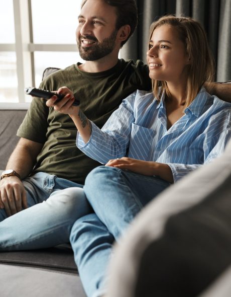 Photo of joyful couple watching TV and using remote control