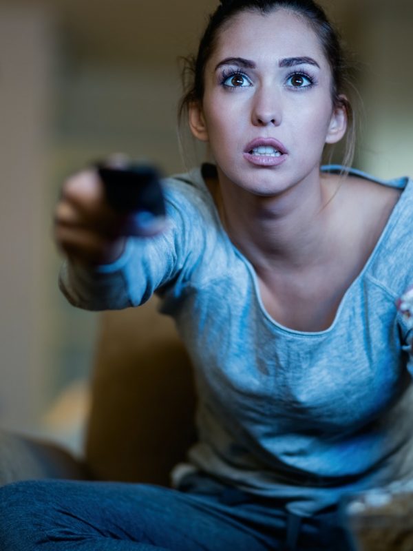 Shocked woman changing channels while watching TV at night.
